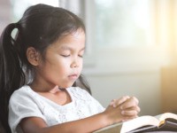 Girl closed her eyes and folded her hand in prayer on a Holy Bible
