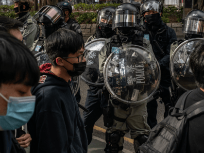 Protesters march on a street as riot police stand guard during a rally against parallel traders in Sheung Shui district on January 5, 2020 in Hong Kong, China. Anti-government protesters in Hong Kong continue their demands for an independent inquiry into police brutality, the retraction of the word "riot" to …