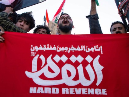 A man holds a slogans in Arabic calling for revenge as the body of Abu Mahdi al-Muhandis,