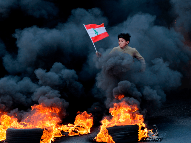 A Lebanese youth runs with a national flag as smoke billows from burning tires during a de