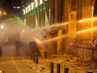 Lebanese protesters take cover as riot police spray them with water from behind a barricaded road leading to parliament in central Beirut on January 19, 2020 amid ongoing anti-government demonstrations. - Lebanese anti-riot police fired rubber bullets and water cannons at stone-throwing demonstrators in the Lebanese capital today, as hundreds …