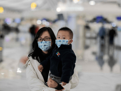 woman and a child wearing protective masks walk toward check-in counters at Daxing interna