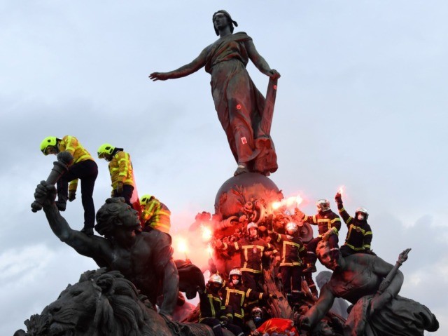 Firefighters brandish flares as they climb on the Statue of Republic Triumph at Nation square during a demonstration to protest against French government's plan to overhaul the country's retirement system in Paris, on January 28, 2020. (Photo by Bertrand GUAY / AFP) (Photo by BERTRAND GUAY/AFP via Getty Images)
