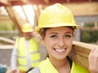 Builder And Female Apprentice Carrying Wood On Site