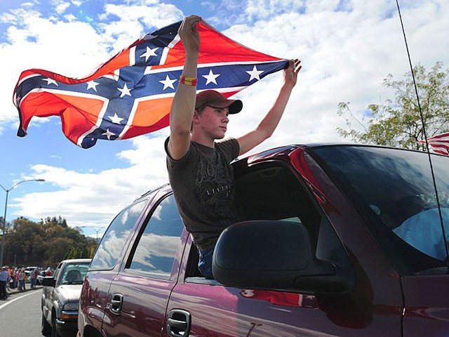 ROSEBURG, OR - OCTOBER 09: Chance White holds a confederate flag as he drives past protesters lining the street in front of the Roseburg Regional Airport on October 9, 2015 in Roseburg, Oregon. Most people turned out to protest President Obama's visit to Roseburg, as the community recovers from last …