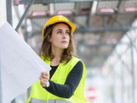 Female construction worker with helmet and safety jacket on construction site examining office blueprints. Outdoors