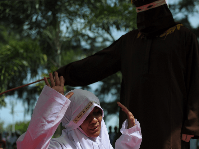 A religious officer canes an Acehnese woman (L) for spending time in close proximity with