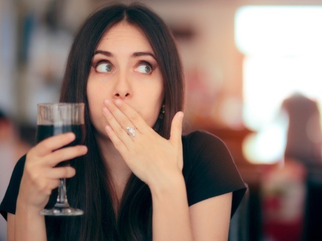 Woman covering her mouth after drinking wine