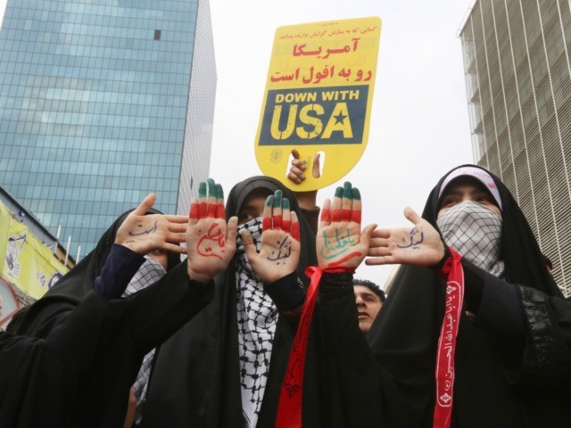 Iranian women display religious symbols written on the palms of their hands under a placar