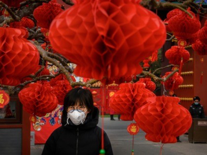 A Chinese woman wears a protective mask as she stands with decorations marking the Chinese New Year holiday at the site of a temple fair that was cancelled on January 26, 2020 in Beijing, China. The number of cases of a deadly new coronavirus rose to over 2000 in mainland …