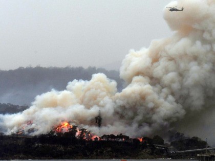 TOPSHOT - A military helicopter flies above a burning woodchip mill in Eden, in Australia's New South Wales state on January 6, 2020. - January 5 brought milder conditions, including some rainfall in New South Wales and neighbouring Victoria state, but some communities were still under threat from out-of-control blazes, …