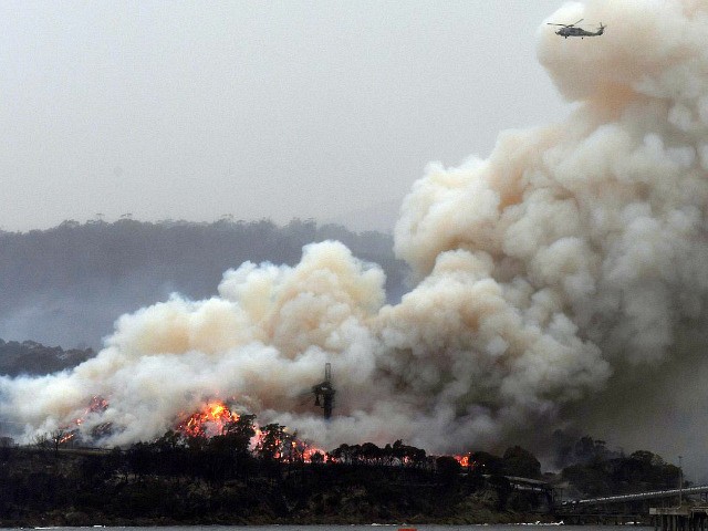 TOPSHOT - A military helicopter flies above a burning woodchip mill in Eden, in Australia'