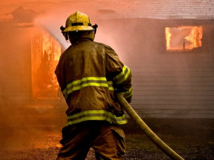 Firefighter spraying water at a house fire - stock photo
