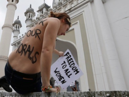 An activist of women's rights organization Femen climbs over a fence in front of a mosque