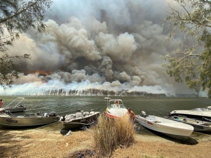Boats are pulled ashore as smoke and wildfires rage behind Lake Conjola, Australia, Thursday, Jan. 2, 2020. Thousands of tourists fled Australia's wildfire-ravaged eastern coast Thursday ahead of worsening conditions as the military started to evacuate people trapped on the shore further south. (Robert Oerlemans via AP)