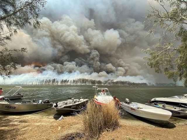 Boats are pulled ashore as smoke and wildfires rage behind Lake Conjola, Australia, Thursd