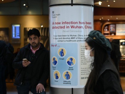 A woman wearing a face mask passes a Public Health England sign, warning arriving passenge