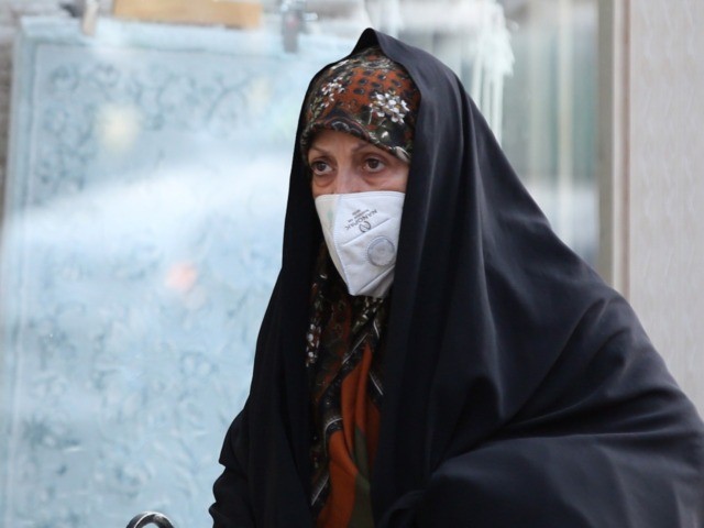 An Iranian woman, wearing a breathing mask while, walks down a street as a blanket of smog