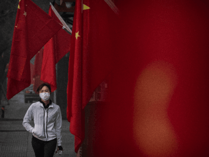 A woman wears a protective mask as she walks by Chinese flags in a street during the Chinese New Year and Spring Festival holiday on January 28, 2020 in Beijing, China. The number of cases of a deadly new coronavirus rose to over 4000 in mainland China Tuesday as health …