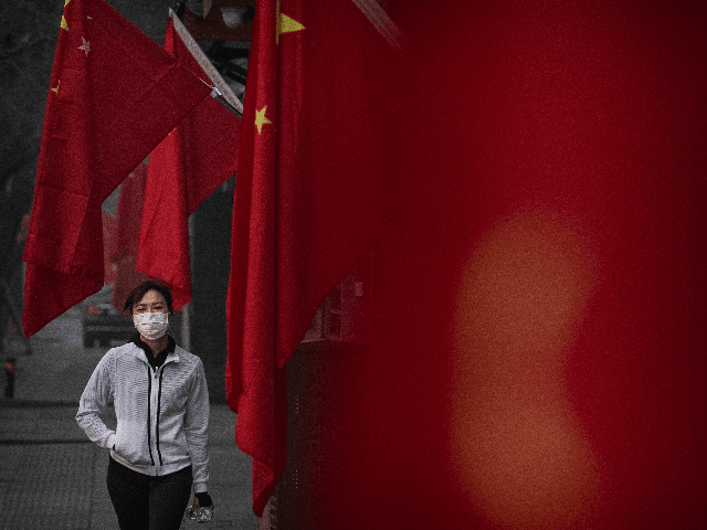 A woman wears a protective mask as she walks by Chinese flags in a street during the Chine