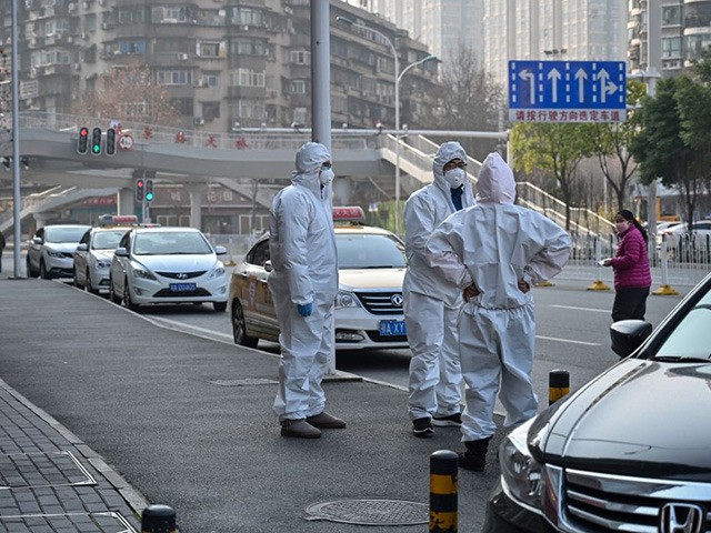 This photo taken on January 30, 2020 shows officials in protective suits gathered on a street after an elderly man wearing a facemask (not pictured) collapsed and died on the pavement near a hospital in Wuhan. - AFP journalists saw the body on January 30, not long before an emergency …