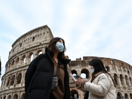 TOPSHOT - Tourists wearing protective respiratory masks tour outside the Colosseo monument
