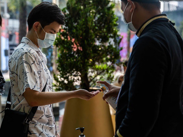 People wearing face-masks visit a hand sanitizer station at Siam Paragon Mall on February