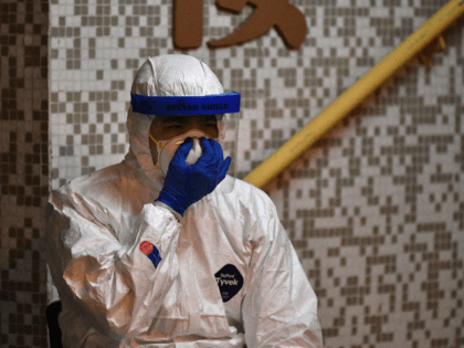 A medical personnel wearing a protective suit checks his mask as he waits near a block's e