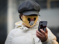A woman wearing a Minnie Mouse face mask looks at her mobile phone in Beijing on February 11, 2020. - The death toll from a new coronavirus outbreak surged past 1,000 on February 11 as the World Health Organization warned infected people who have not travelled to China could be …