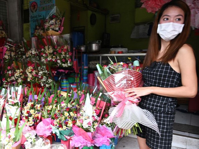 A vendor wearing a protective facemask stands at their shop on Valentine's day at a flower