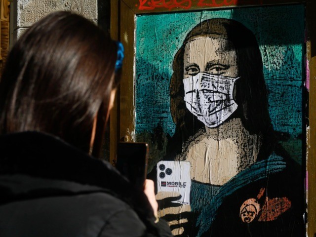 A woman takes a picture with her mobile phone of a poster by Italian urban artist Salvator