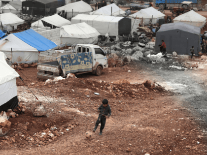 A Syrian boy plays with a football at a makeshift camp for displaced people who fled pro-r