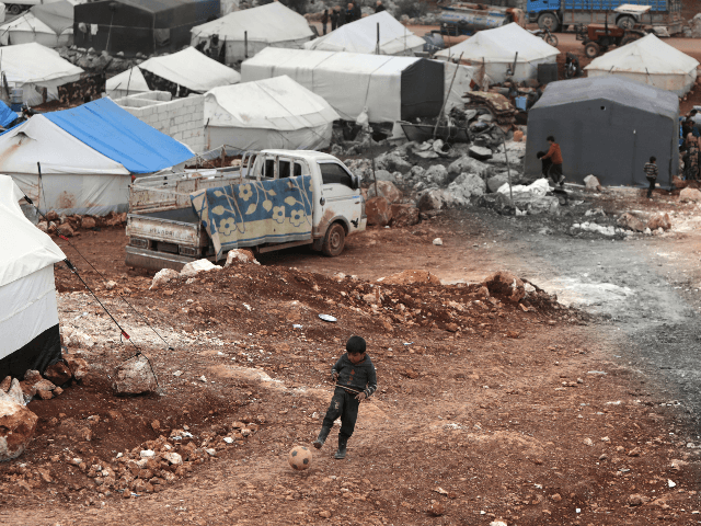 A Syrian boy plays with a football at a makeshift camp for displaced people who fled pro-r