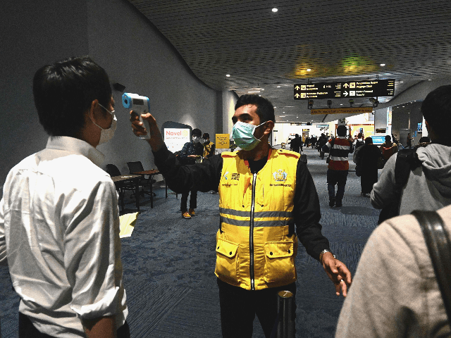 An Indonesian health officials takes temperature readings of arriving passengers amid conc
