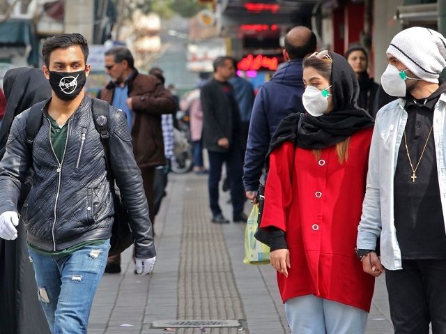 A man wears a protective mask bearing the logo of the US' National Aeronautics and Space Administration (NASA) while walking with others also wearing masks along a street in the Iranian capital Tehran on February 24, 2020. - Iran's government vowed on February 24 to be transparent after being accused …