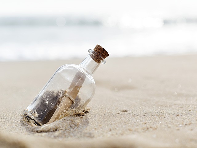 closeup of a glass bottle with a rolled message inside stranded in the sand of a lonely be