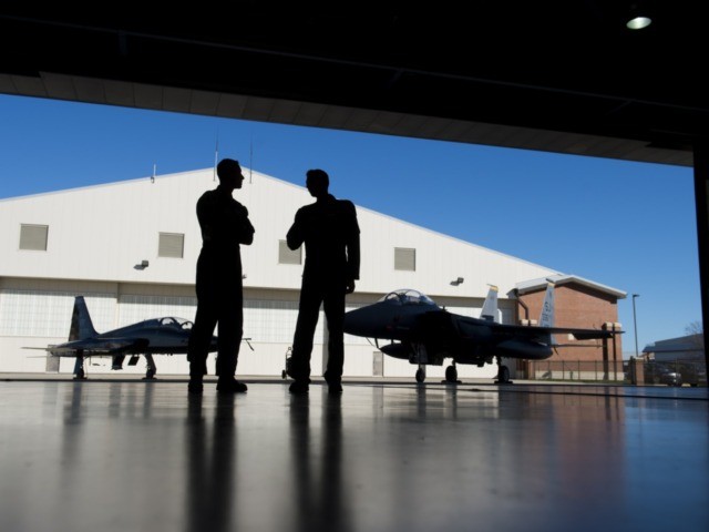 Pilots with the US Air Force stand inside a hangar alongside a F-15 fighter jet and a T-38