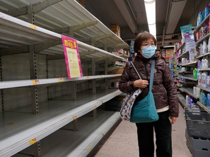 A woman wearing face mask walks past empty shelf of tissue papers at supermarket in Hong K
