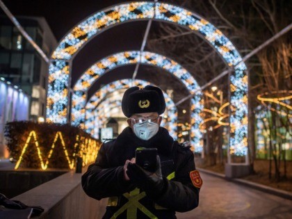 A security guard, wearing a protective facemask to protect against the COVID-19 novel coronavirus, browses his mobile phone as he secures the entrance of a nearly empty shopping mall in Beijing on February 27, 2020. - The novel coronavirus has spread to more than 25 countries since it emerged in …