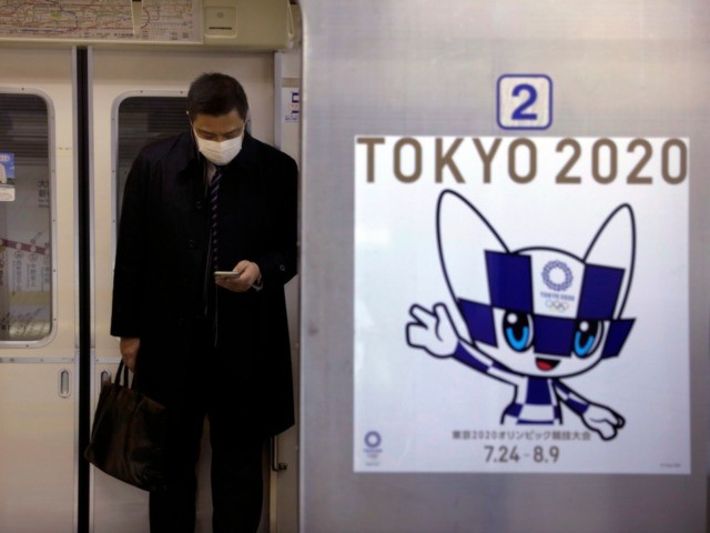 A poster promoting the Tokyo 2020 Olympics is posted next a train door as a commuter weari