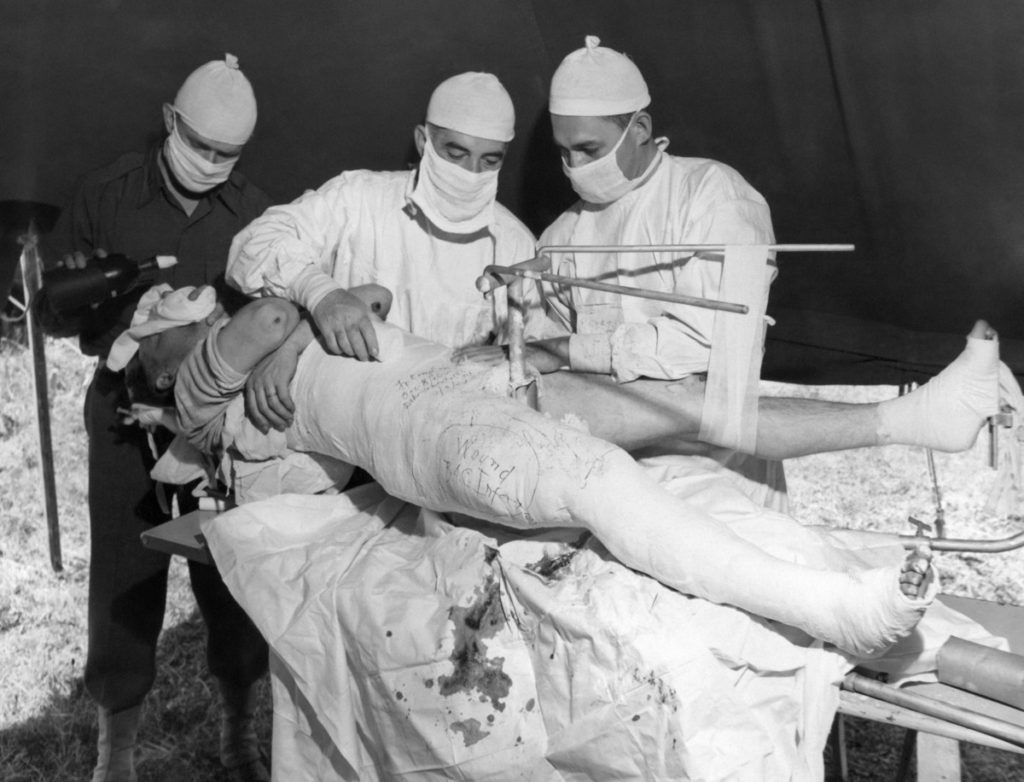 Using 180,000 units of anti-toxin penicillin and sulpha diazine, members of the U.S. Army Medical Corps treat a German prisoner at an evacuation hospital in Brittany, France on September 26, 1944 for gas gangrene, which has set in a rifle bullet wound which shattered the patients thigh bone above the knee. The anesthetist is Captain Fred Ivons of Lexington, Virginia; the surgeon is Major John Curley of Leomister, Massachusetts, and the assistant surgeon Captain James D. Woodruff of Baltimore, Maryland. A diagram of the fracture is drawn on the cast. The patient was taken prisoner near Brest and claimed to be an anti-Nazi. (AP Photo/George Greb)