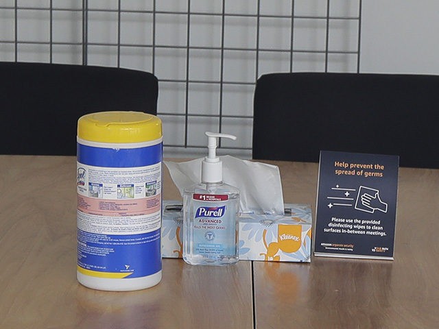 Hand sanitizer, cleaning wipes, and tissues sit on a meeting room table as seen through a