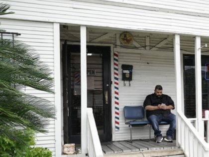 Barber Carlos Vasquez sits on the porch of his family's barber shop as he waits for a customer Friday, March 20, 2020, in Houston. Vasquez estimates their business has dropped in half since the coronavirus outbreak. (AP Photo/David J. Phillip)