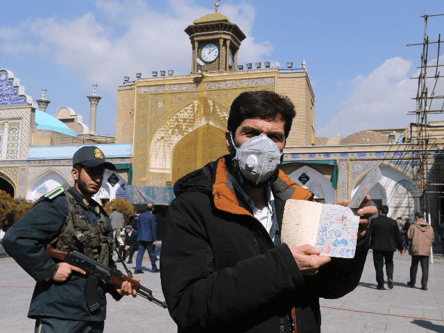 An Iranian voter wears a mask and shows his ID during parliamentary elections at the Shah