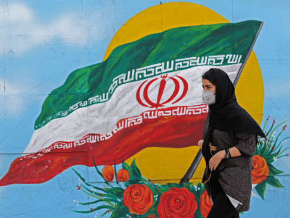 Iranians wearing masks walk past a mural displaying their national flag in Tehran on March