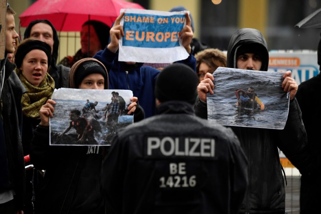 German police face demonstrators holding up pictures of refugees as they demonstrate against Europe's migration policy and the handling of refugees at the Greek border on March 9, 2020 opposite the venue of a German-Hellenic Economic Forum in Berlin. (Photo by John MACDOUGALL / AFP) (Photo by JOHN MACDOUGALL/AFP via Getty Images)