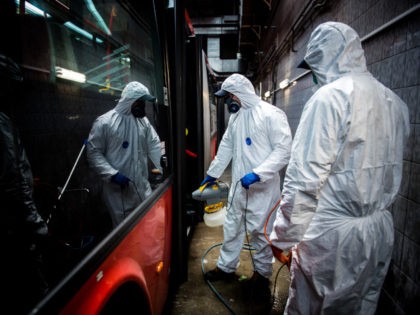 Workers wearing protective clothes disinfect an interior of a public bus in a bus-wash sta