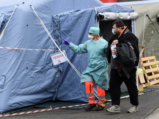 A hospital employee wearing a protection mask and gear, escorts a patient towards the radiology unit at a temporary emergency structure set up outside the accident and emergency department, where any new arrivals presenting suspect new coronavirus symptoms are being tested, at the Brescia hospital, Lombardy, on March 13, 2020. …