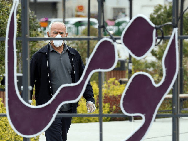 A man wearing a protective face mask and plastic gloves walks along a street in Iran's cap
