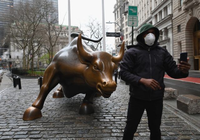 A man wearing a face mask takes a selfie at the Charging Bull statue on March 23, 2020 near the New Stock Exchange in New York City. - Wall Street fell early March 23, 2020 as Congress wrangled over a massive stimulus package while the Federal Reserve unveiled new emergency …